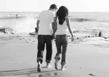 Un hombre y una mujer caminan  por la orilla del mar cogidos de la mano